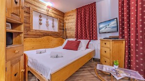 Quarto de madeira com uma cama, uma televisão e um jornal sobre a mesa.