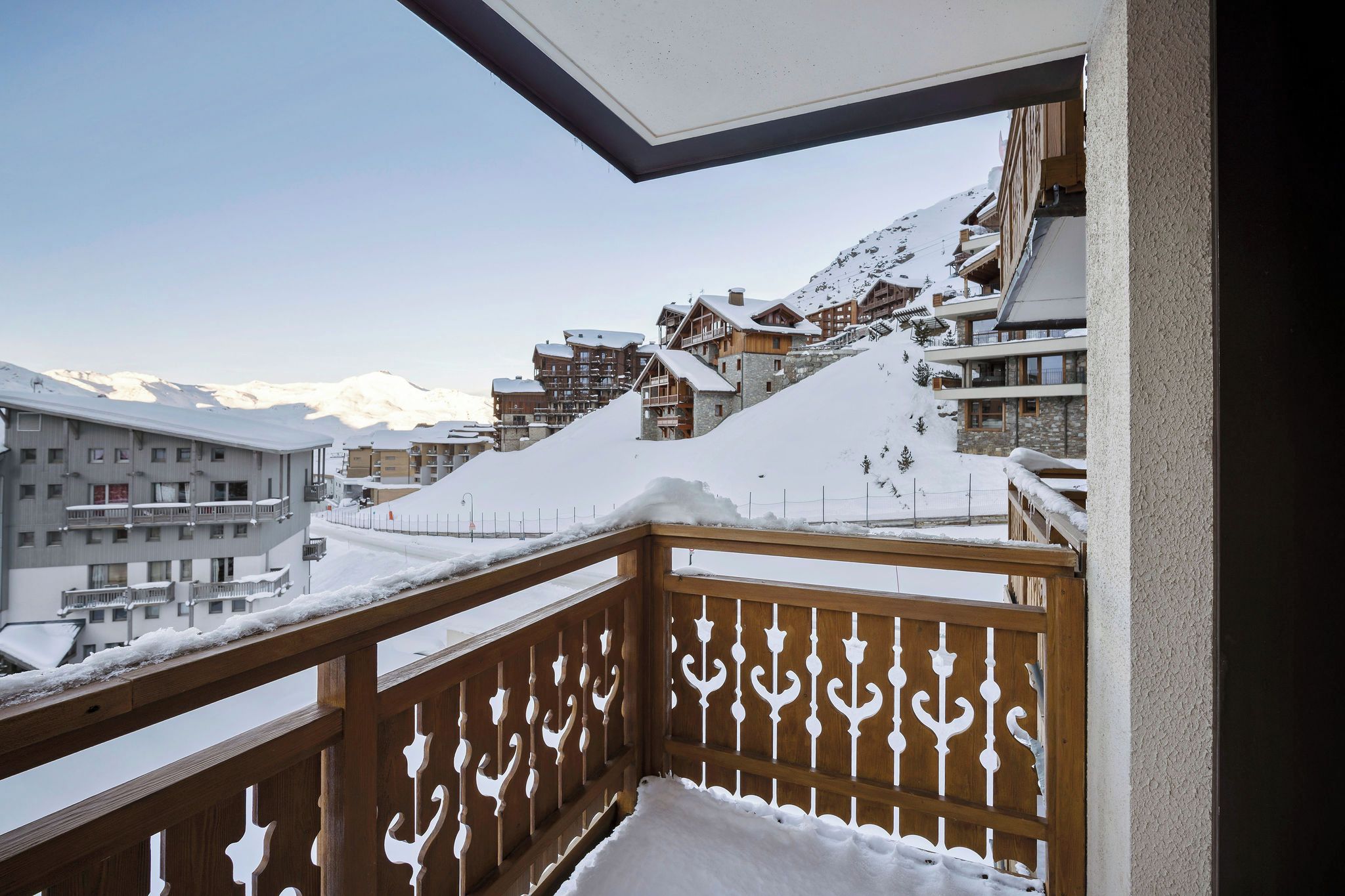 Un balcón cubierto de nieve con vistas a un complejo turístico de montaña.