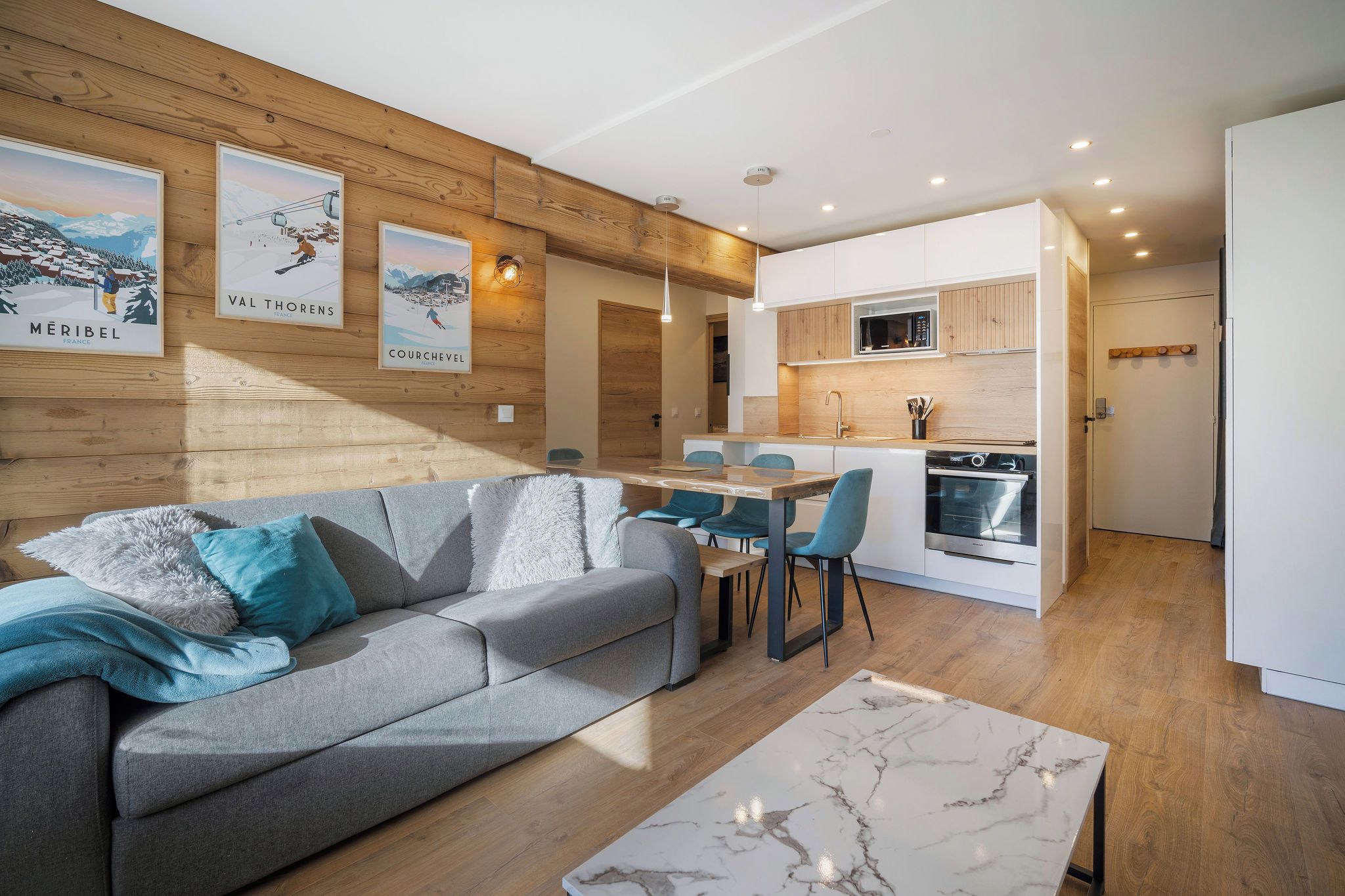 Una sala de estar moderna con un sofá gris, una mesa de comedor de madera con sillas, y una cocina con armarios blancos y un microondas.