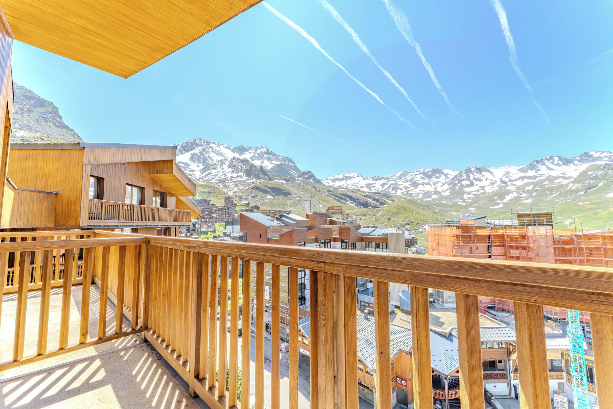 A wooden balcony overlooking a mountainous landscape with snow-capped peaks and a clear sky.