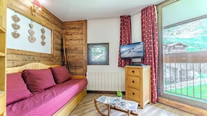 Una habitación con pared de madera, una cama con ropa de cama roja, un aparador de madera, un televisor y una ventana con vistas.