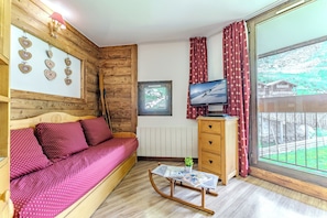Una habitación con pared de madera, una cama con ropa de cama roja, un aparador de madera, un televisor y una ventana con vistas.