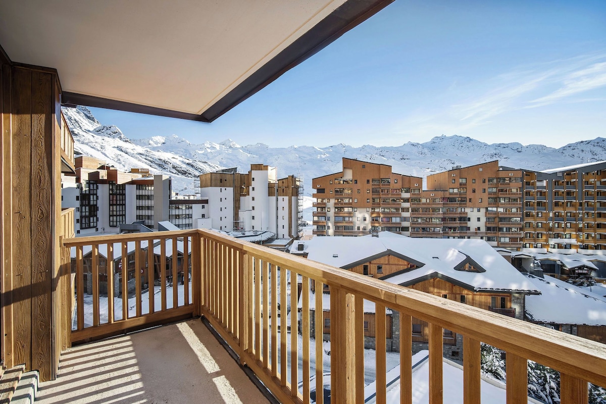 A balcony with a wooden railing overlooking a snow-covered mountain landscape and modern buildings.