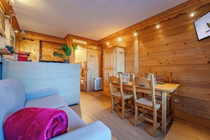 A cozy room with a sofa, a dining table with chairs, wooden walls, and a ceiling with lights. - La Roche Blanche Val Thorens (Les Belleville)