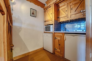 A compact kitchen with wooden cabinets, a microwave, a dishwasher, and a tiled backsplash.