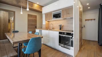 A modern kitchen with white cabinets, a built-in microwave, and a stainless steel oven. There is a wooden dining table with blue chairs.