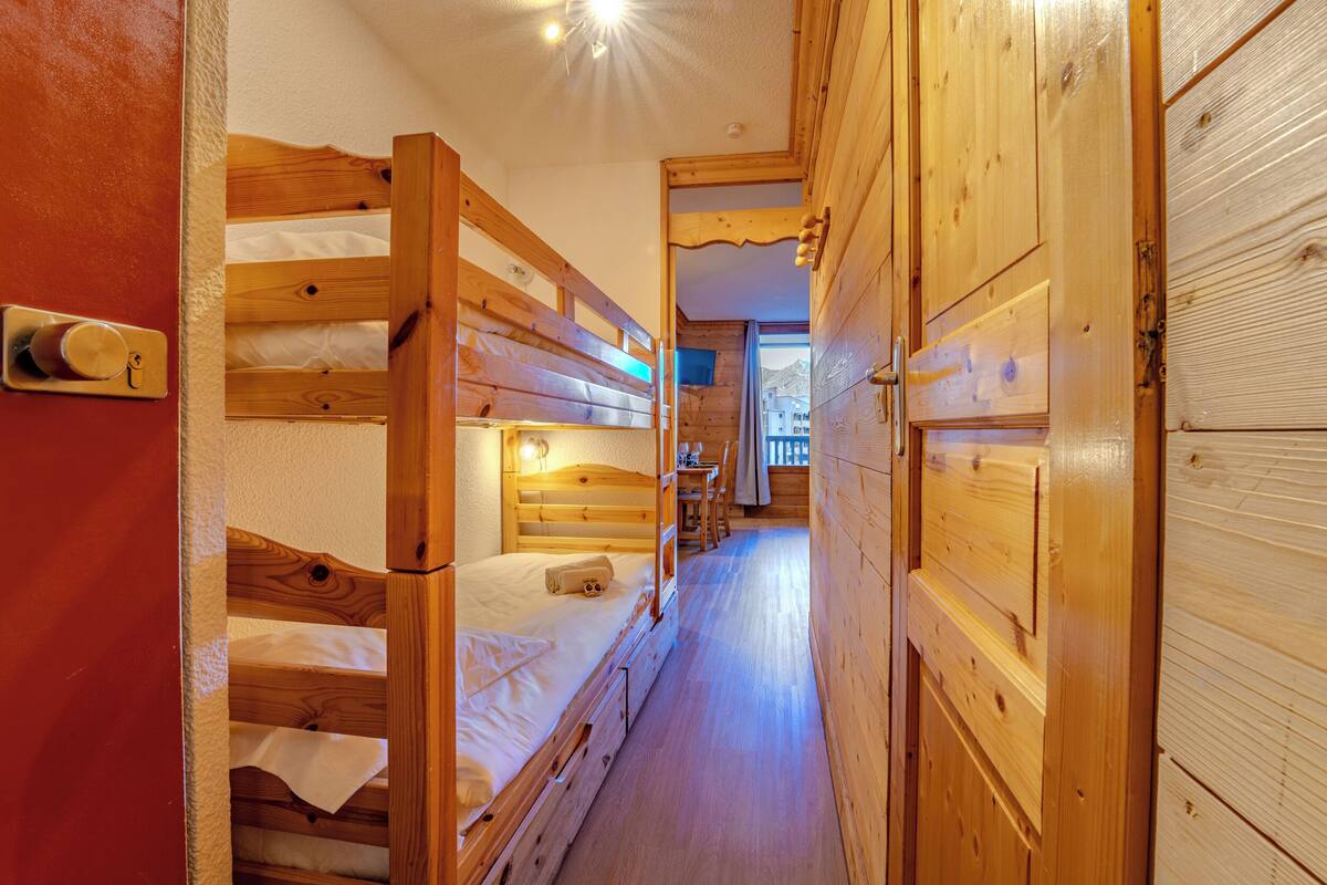Un intérieur en bois avec des lits superposés, une porte en bois et un couloir menant à une autre pièce.