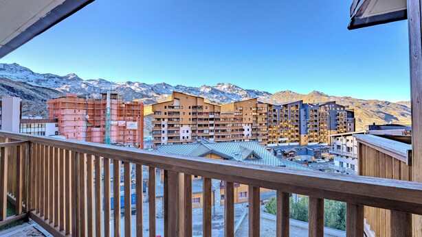 Vista de un hotel con varias edificaciones, un balcón de madera y montañas al fondo.