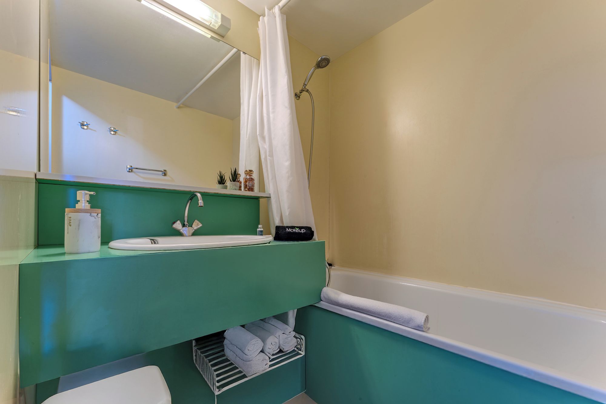 A bathroom with a green vanity, a white sink, a mirror, a shower, and a towel rack.