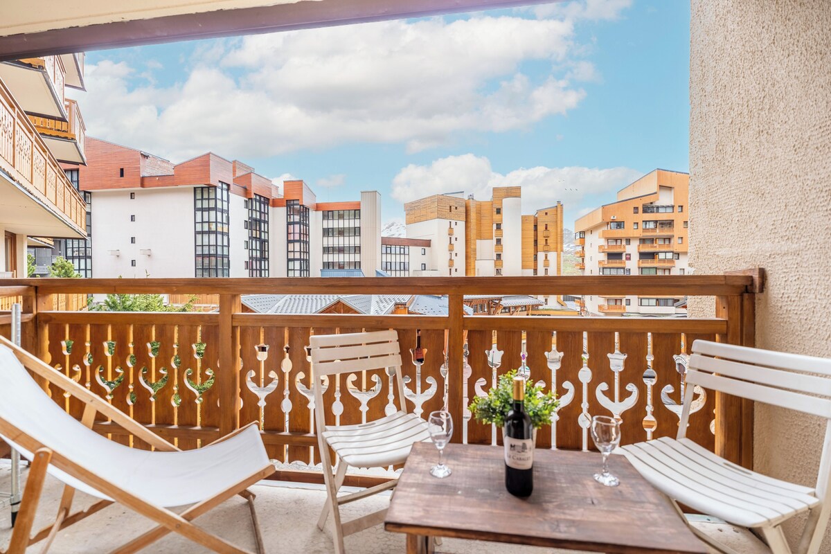 A balcony with white chairs and a table, overlooking a cityscape with modern buildings.