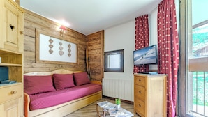 Um quarto aconchegante com uma cama de madeira, uma mesinha com uma planta, uma televisão e uma janela com cortinas.
