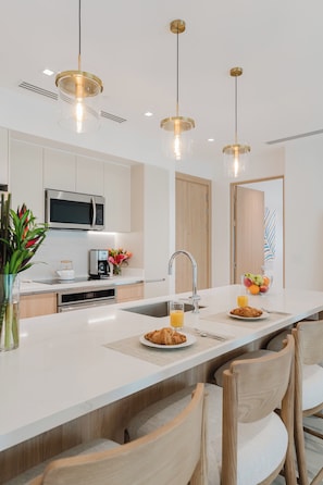 Une cuisine moderne dotée d’un îlot central, d’appareils électroménagers en acier inoxydable et de luminaires suspendus.