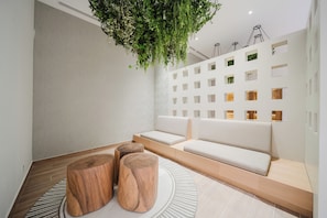 A modern interior with a seating area, wooden stools, a hanging plant, and a wall with multiple small windows. - Step Into Unparalleled Luxury and Expansive Comfort at our Signature Residences (Telire)