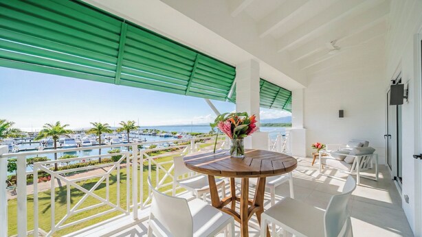 A balcony with a wooden table and chairs, a vase with flowers, and a view of a pool and greenery. - Step Into Unparalleled Luxury and Expansive Comfort at our Signature Residences (Quepos)