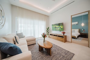 A modern living room with a sofa, coffee table, TV, and a bedroom with a bed and dresser.