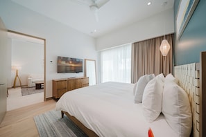 A modern hotel room with a large bed, a flat-screen TV, a wooden dresser, and a view of the outdoors through the window. - Discover Unparalleled Elegance at our Marina Vista Villas! (Telire)