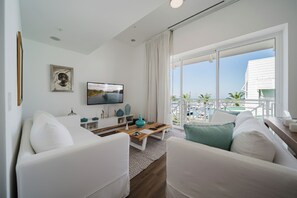 A modern living room with a TV, white sofas, a wooden coffee table, and a balcony with outdoor furniture. - Discover the Pinnacle of Luxury and Serenity With La Costa! (Telire)