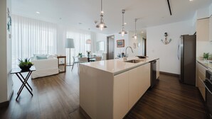 A modern kitchen with a central island, wooden flooring, pendant lighting, and a dining area with a white sofa and table. - Discover the Pinnacle of Luxury and Serenity With La Costa! (Quepos)