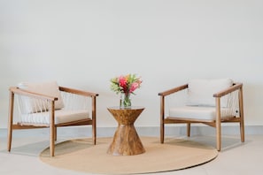 Två trästolar med kuddar, ett runt träbord med en vas med blommor och en beige matta på ett klinkergolv.