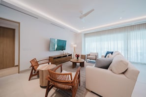 A modern living room with a sofa, chairs, a coffee table, a TV, and a large window with curtains. - Experience Expansive Luxury at our Gran Costa Villas! (Telire)