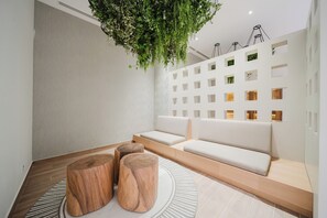 A modern interior with a seating area, wooden stools, a hanging plant, and a wall with multiple small windows. - Experience Expansive Luxury at our Gran Costa Villas! (Telire)