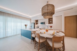A modern kitchen with a central island, a dining area with chairs, and a large window with sheer curtains. - Experience Expansive Luxury at our Gran Costa Villas! (Telire)