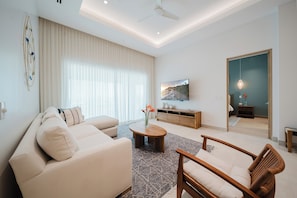 A modern living room with a sofa, armchair, coffee table, and a TV on a wooden cabinet.
