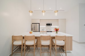 A modern kitchen with a central island, wooden chairs, and pendant lighting. - Experience the Ultimate in Spacious Luxury at our Panorama Villas! (Telire)