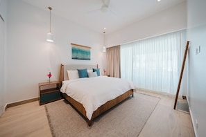 A modern bedroom with a large bed, a nightstand, a ceiling fan, and a window with sheer curtains. - Experience the Ultimate in Spacious Luxury at our Panorama Villas! (Telire)