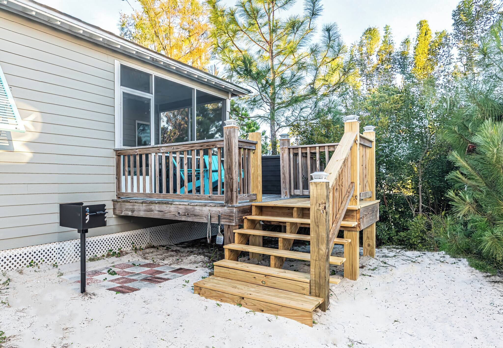 A wooden deck with a mailbox, a house with a screened porch, and a sandy ground.