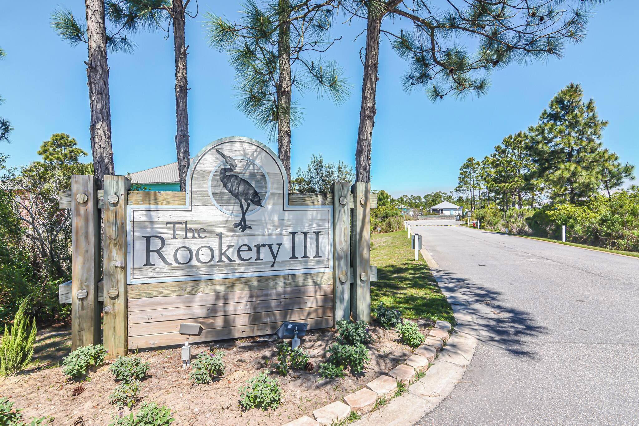 A wooden sign with a bird and the text 'The Rookery III' in a rural setting with trees and a road.