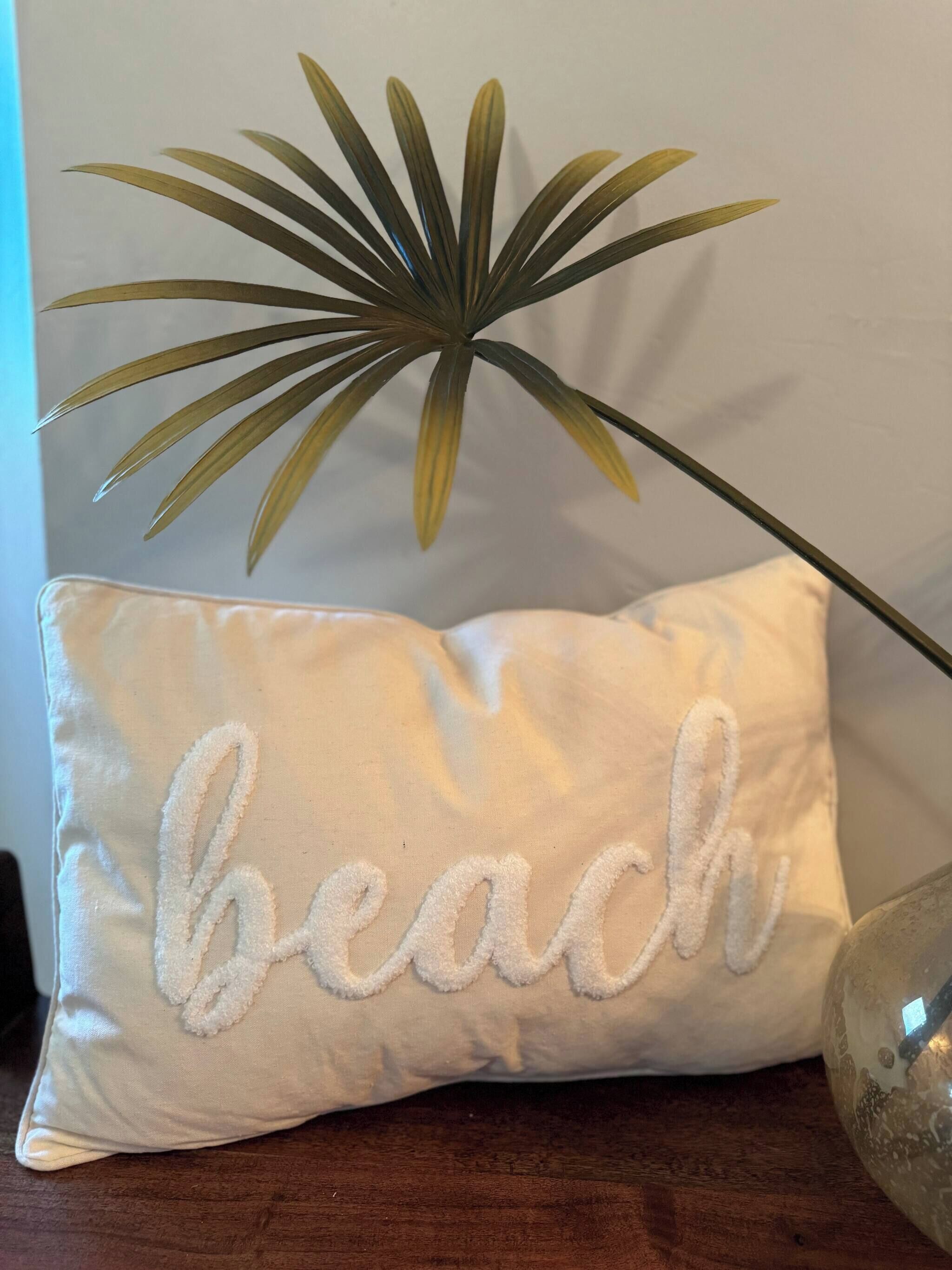 A pillow with the word 'beach' embroidered on it, placed on a wooden surface.