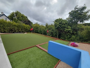 Ein Croquet-Platz mit zwei roten Markierungsfahnen, umgeben von Hecken und Bäumen.