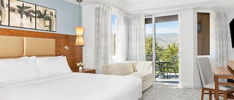 A hotel room with a large bed, a sofa, a desk, and a balcony with a view of the mountains.