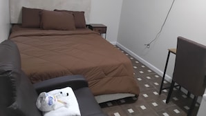 A bedroom with a bed, a TV mounted on the wall, a small table, and a chair. - Log Comfort 3 (Newark)