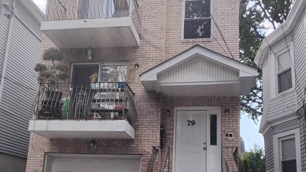 A two-story brick house with a garage, a front door labeled '79', and a staircase leading to the entrance. - Log Comfort 3 (Newark)