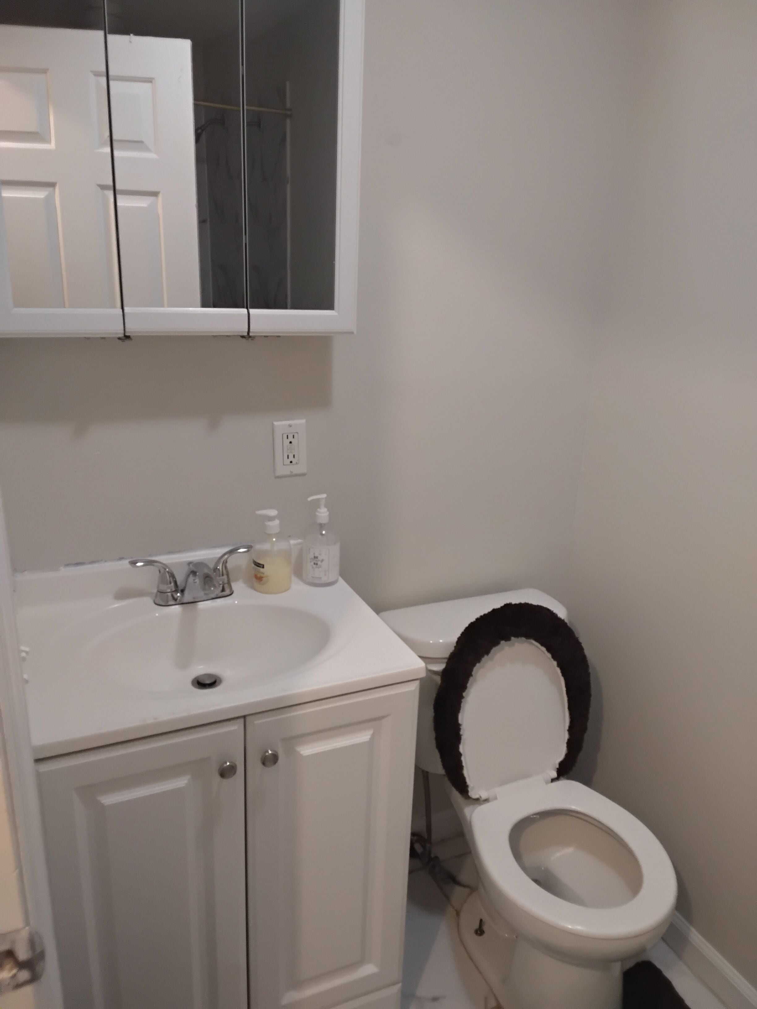 Un baño con un lavamanos blanco, un inodoro, un espejo sobre el lavamanos y una puerta.