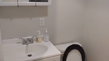 Un baño con un lavamanos blanco, un inodoro, un espejo sobre el lavamanos y una puerta.