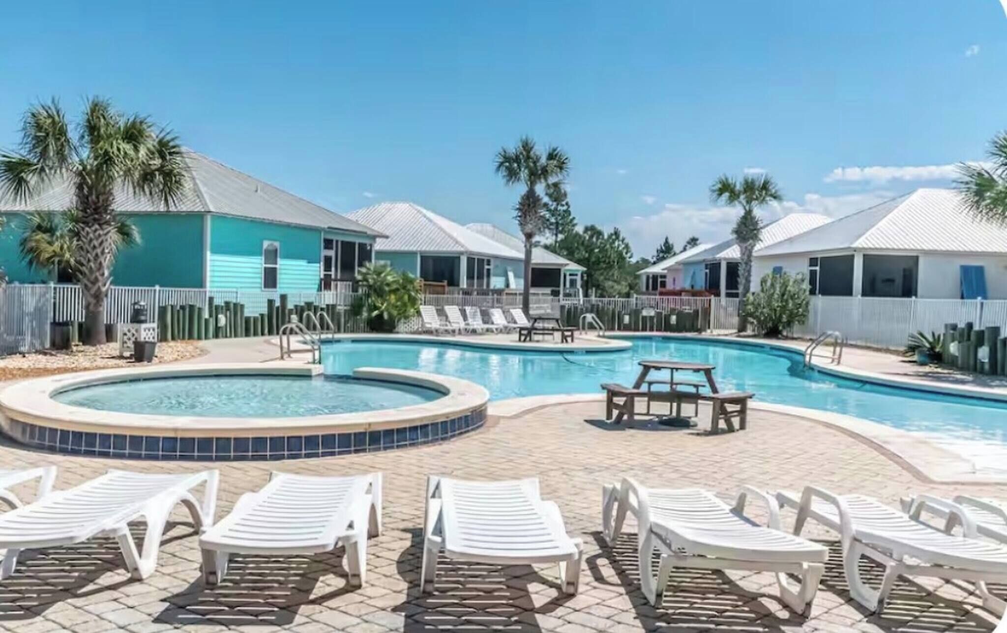 Zona de piscina con sillas de descanso y un jacuzzi, rodeada de casas con tejados blancos.