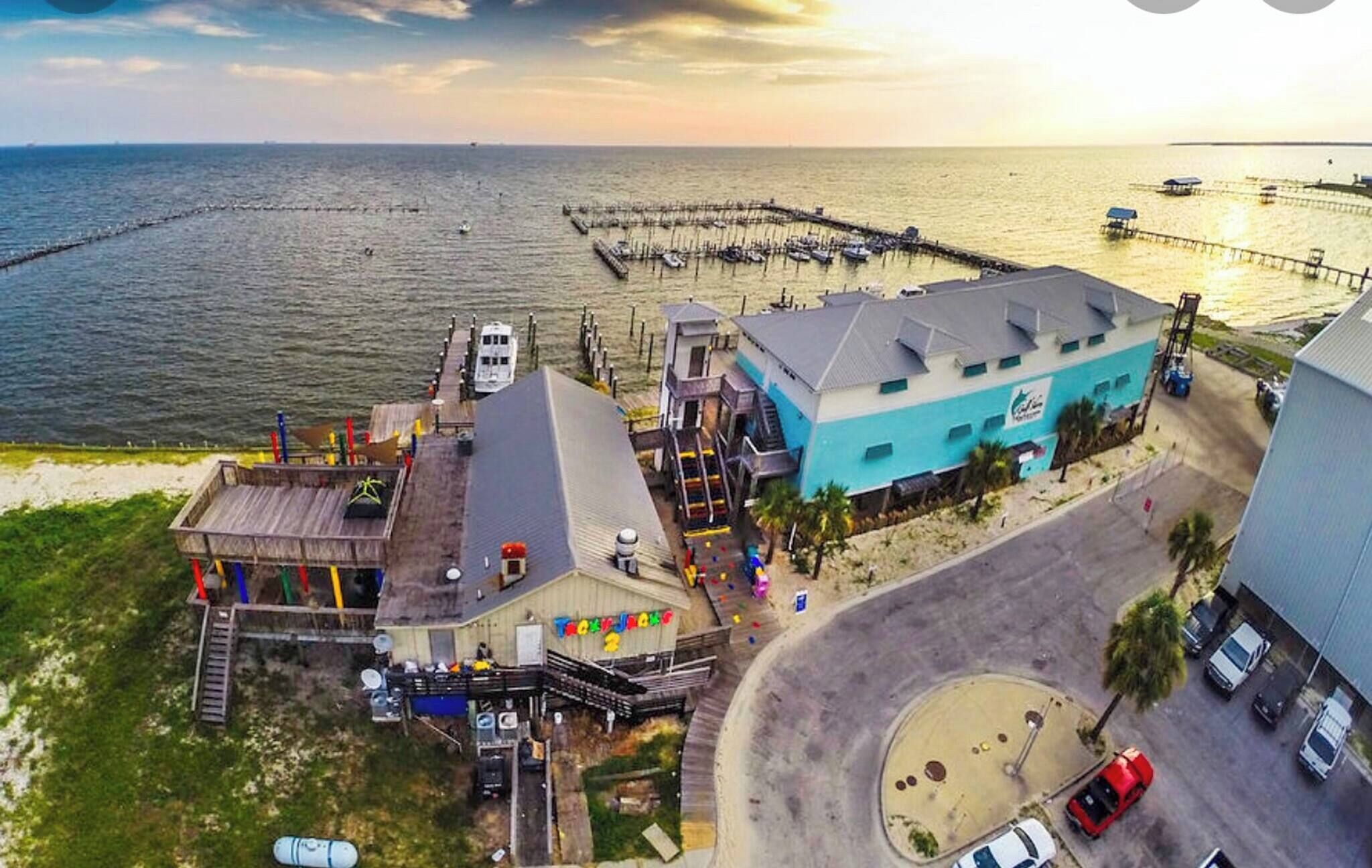 Un hotel sulla costa con un molo che si protende nell'acqua, un'area parcheggio e un edificio con facciata blu.