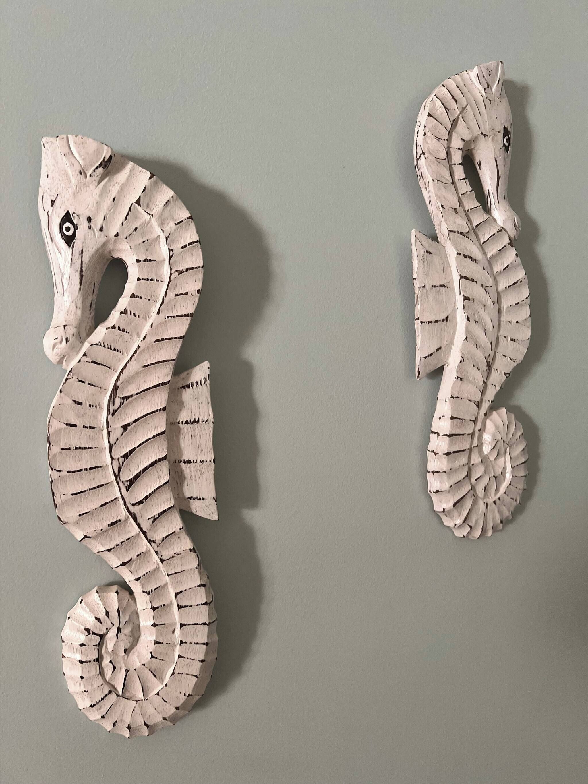 Two white seahorse sculptures on a plain wall.