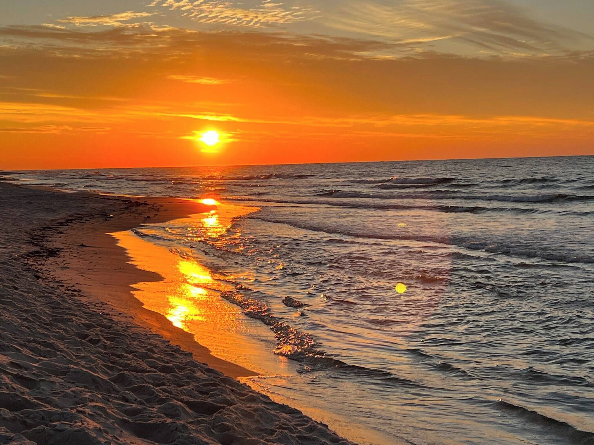 A beach with a sunset, waves, and a sandy shoreline.