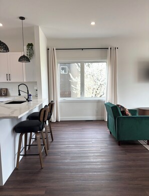 A modern kitchen with a central island, bar stools, a green sofa, and a large window with curtains.