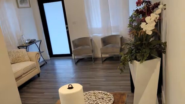 Una sala moderna con una mesa de comedor de madera, dos sillas, un jarrón blanco con flores y un ventilador de techo.