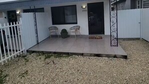 Un edificio con un patio techado, cerca blanca y suelo de grava.