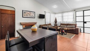 Una sala de estar con una mesa de comedor, dos sofás, un televisor y un ventanal con cortinas.