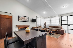Una sala de estar con una mesa de comedor, dos sofás, un televisor y un ventanal con cortinas.