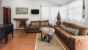 Una sala de estar con chimenea, sofás marrones, una mesa de centro y un televisor montado en la pared.
