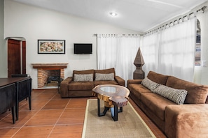 Una sala de estar con chimenea, sofás marrones, una mesa de centro y un televisor montado en la pared.