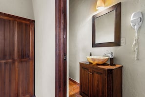 Una puerta de madera, un baño con tocador de madera, un espejo y un secador de pelo montado en la pared.